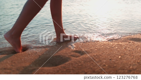 Person strolling sunset sandy shore. Slim female legs walking ocean water waves sand beach. Woman barefoot on seaside surf in sunrise light. Girl tourist on summer vacation on tropical island resort. Person strolling sunset sandy shore. Slim female legs walking ocean water waves sand beach. Woman barefoot on seaside surf in sunrise light. Girl tourist on summer vacation on tropical island resort. 123276768