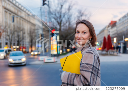 Happy woman portrait holding yellow folder papers document letter on european busy Berlin Mitte city street twilight evening night. Female student business person journey visiting Germany capital Happy woman portrait holding yellow folder papers document letter on european busy Berlin Mitte city street twilight evening night. Female student business person journey visiting Germany capital 123277009