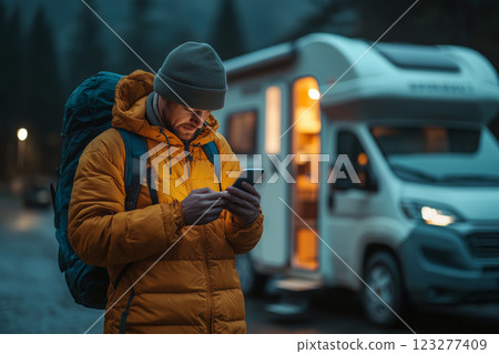 Caucasian male checks phone while standing by RV during twilight hours 123277409