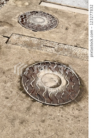 A dirty rusty iron hatch with a pattern is located next to dry grass during the daytime. The water is on the surface of the hatch. Close-up 123277832