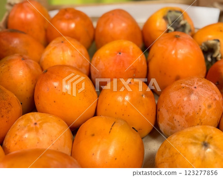 A pile of ripe juicy orange persimmons in a box, on sale at a supermarket vegetable stand, showcases organic, vegetarian and healthy food. Close-up. 123277856