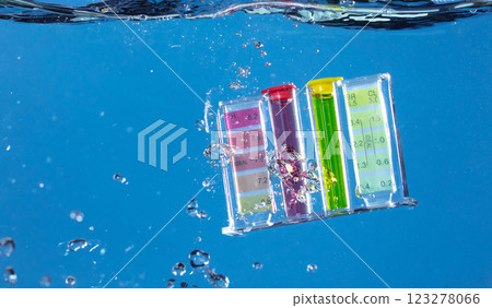 PH acid level test kit on quality water on screen. PH acid level tester kit tools fall under water splashing splattering with air bubble over blue background isolated 123278066