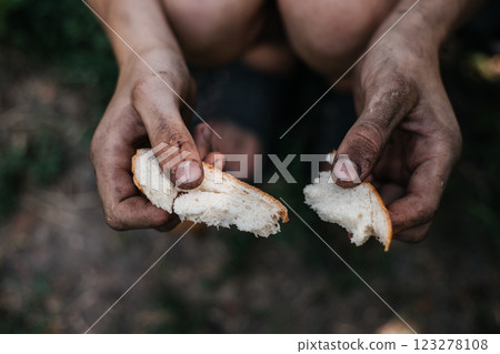 Homeless poor man holds a piece of white bread in his dirty hands. It is a symbol of poverty and hunger in modern society. Homeless poor man holds a piece of white bread in his dirty hands. It is a symbol of poverty and hunger in modern society. 123278108