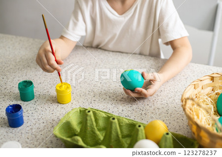 The hands of a child coloring eggs with a brush. Nearby are paints and a wicker basket. Easter 123278237