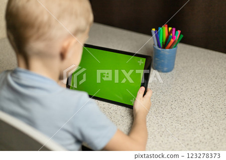 The child is sitting at the table, playing and looking at the tablet on the green screen. Chromakey The child is sitting at the table, playing and looking at the tablet on the green screen. Chromakey 123278373