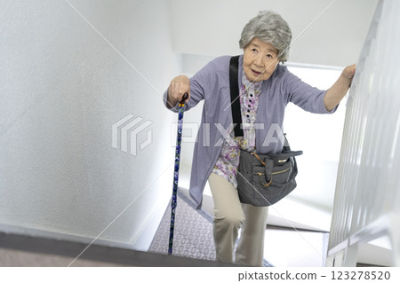 A woman in her 80s walking up the stairs with a cane 123278520