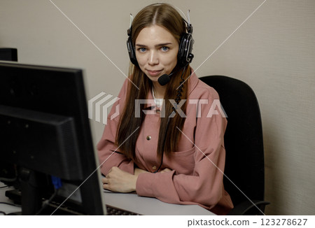 A happy call center agent working on a support hotline in the office. Close-up. A telemarketer, a telemarketing agent, makes a conference video call, talks to an online client on a computer. A happy call center agent working on a support hotline in the office. Close-up. A telemarketer, a telemarketing agent, makes a conference video call, talks to an online client on a computer. 123278627
