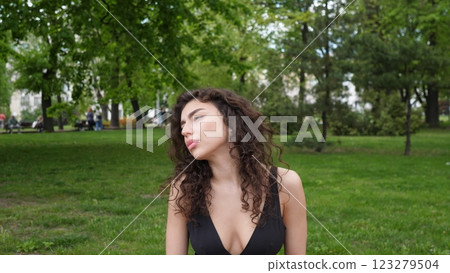 A woman with beautiful curly hair reflects thoughtfully in a serene park setting, surrounded by lush greenery A woman with beautiful curly hair reflects thoughtfully in a serene park setting, surrounded by lush greenery 123279504