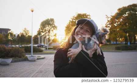 A smiling woman gently holds her small dog close to her, beautifully captured during a stunning sunset A smiling woman gently holds her small dog close to her, beautifully captured during a stunning sunset 123279539
