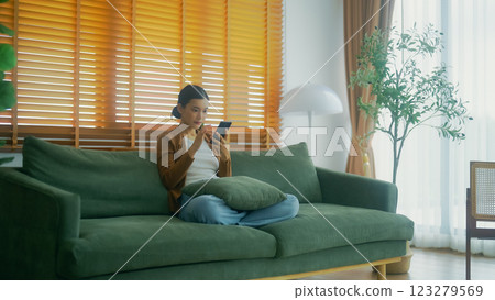 Smiling pretty young Asian woman sitting on cozy couch 123279569