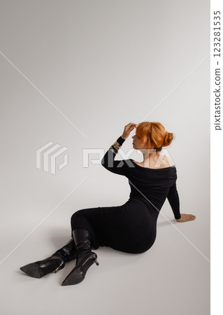 Elegant red hear woman in black dress lying on white background. Back view. Elegant red hear woman in black dress lying on white background. Back view. 123281535