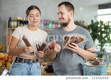 Spouses looking at hamon and dried sausage in store 123282018