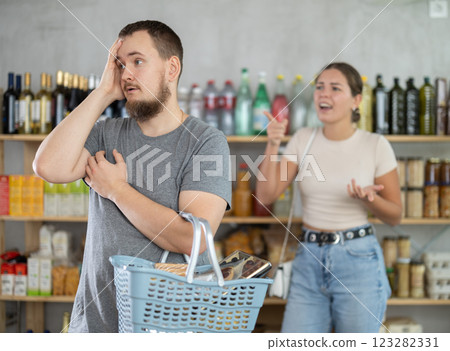 Wife stands behind husband and yells at companion in shop Wife stands behind husband and yells at companion in shop 123282331