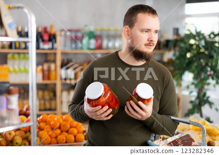Man carefully selects canned tomatoes in the produce section of supermarket Man carefully selects canned tomatoes in the produce section of supermarket 123282346