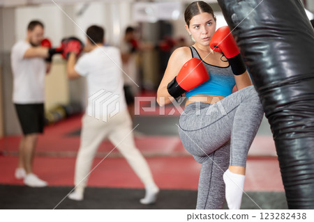 Girl punches and kicks punching bag in gym. Girl punches and kicks punching bag in gym. 123282438