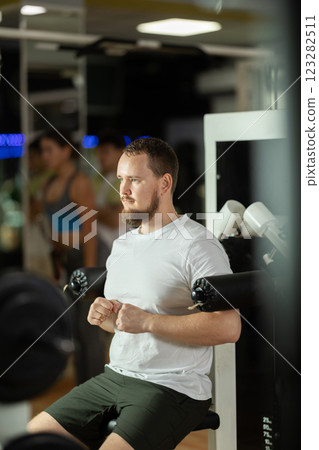 Bearded man in gym performs exercises for arm muscles using simulators and fitness center equipment. 123282511