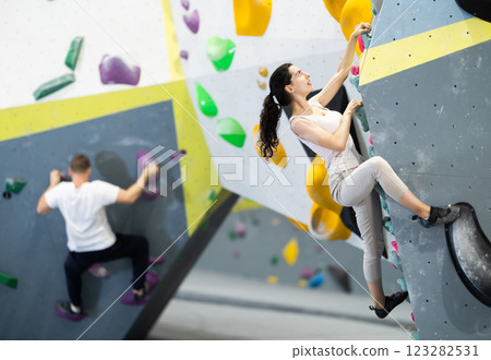 Motivated young girl climbing without ropes and harnesses on artificial bouldering wall in fitness center 123282531