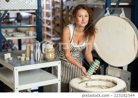 Female potter takes finished clay pottery out of oven 123282544