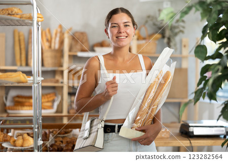 Positive young girl holding baguettes in plastic bag in bakery Positive young girl holding baguettes in plastic bag in bakery 123282564