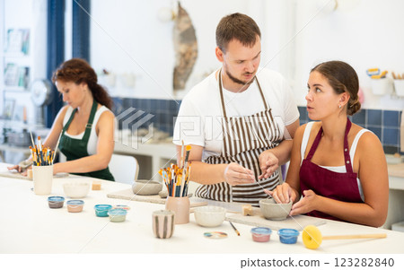 Pupils are sitting near work table, sculpting plate of raw clay under supervision of male teacher Pupils are sitting near work table, sculpting plate of raw clay under supervision of male teacher 123282840