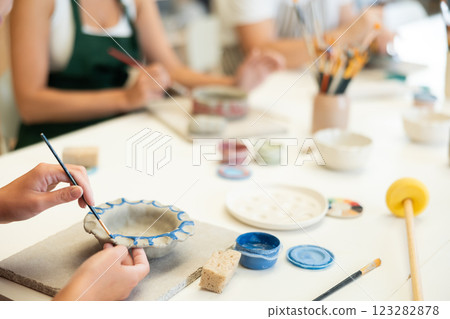 Closeup of female hands painting ceramic plate with paint and brush in pottery workshop 123282878