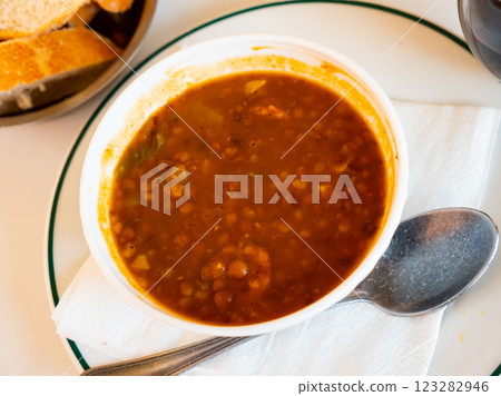 Spicy stewed lentils with suasage and vegetables with thick tomato sauce served in white plate. Spanish cuisine 123282946