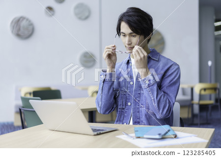 A young man wearing glasses operating a laptop computer in an office cafe. Photo courtesy of Sky Perfect Tokyo Media Center 123285405