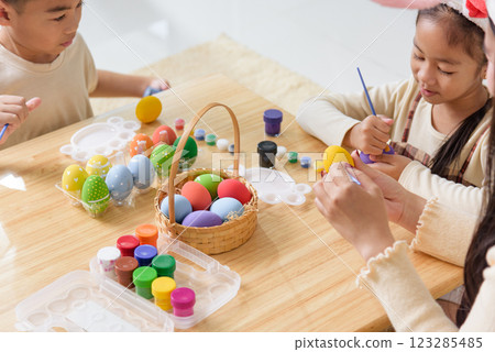 Easter fun for all. Kids with bunny ears joyfully paint Easter eggs with brushes 123285485