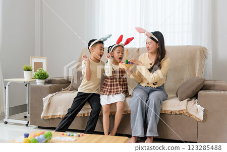 Easter family joy. A cheerful mother and kids with bunny ears celebrate Easter at home Easter family joy. A cheerful mother and kids with bunny ears celebrate Easter at home 123285488