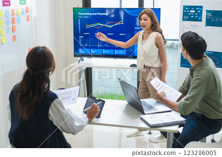 asian leader presenting a financial data and strategies in a modern office with charts and graphs displayed on a large screen 123286005