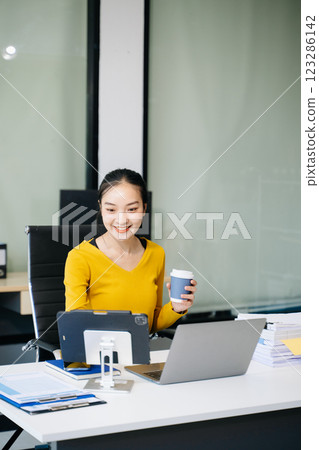 Asian Businesswoman Analyzing Finance on Tablet and Laptop at modern Office Desk tax 123286142
