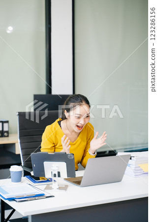 Asian Businesswoman Analyzing Finance on Tablet and Laptop at modern Office Desk tax 123286156