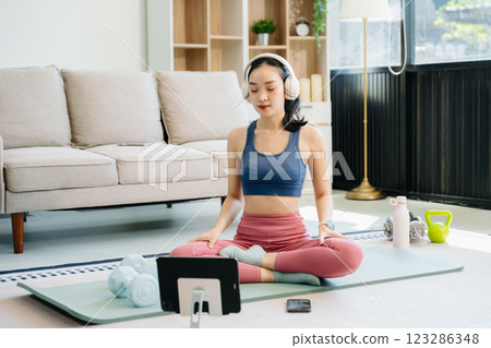 Asian Woman Doing Yoga and Watching Online Tutorials on tablet, Training 123286348