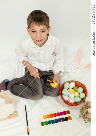 Little Boy with Easter Bunny Ears Painting Easter Eggs on White Background 123286419