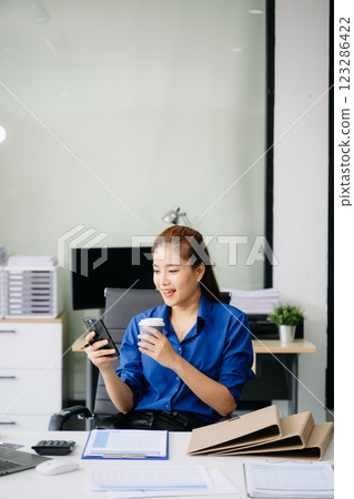 Confident beautiful Asian businesswoman typing laptop computer and digital tablet while holding coffee Confident beautiful Asian businesswoman typing laptop computer and digital tablet while holding coffee 123286422