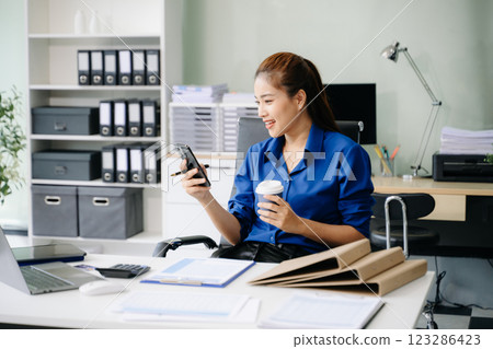 Confident beautiful Asian businesswoman typing laptop computer and digital tablet while holding coffee Confident beautiful Asian businesswoman typing laptop computer and digital tablet while holding coffee 123286423