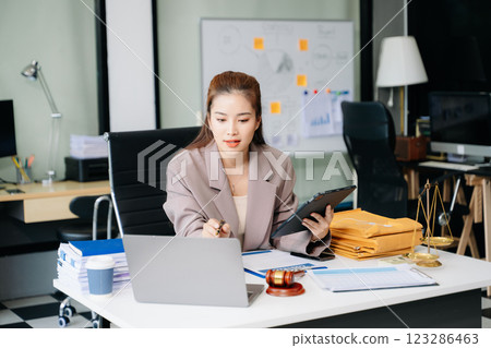 Confident lawyer working on legal analysis at a modern office desk, featuring scales of justice, a gavel 123286463