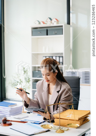 Confident lawyer working on legal analysis at a modern office desk, featuring scales of justice, a gavel Confident lawyer working on legal analysis at a modern office desk, featuring scales of justice, a gavel 123286465