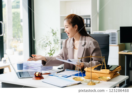 Confident lawyer working on legal analysis at a modern office desk, featuring scales of justice, a gavel 123286488