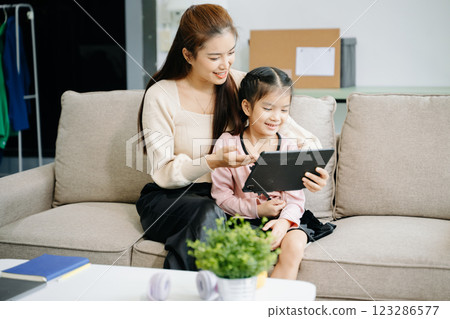 Cheerful mother and daughter sharing quality time on a couch, smiling and using a smartphone together. 123286577