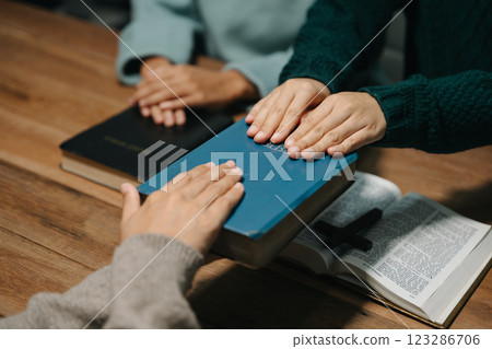 Group of Christians sit together and pray around a wooden table with blurred open Bible pages in their homeroom. Prayer for brothers, faith, hope, a 123286706