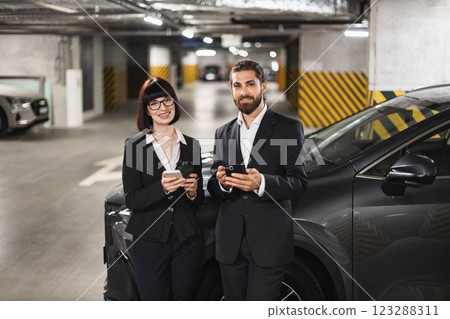 Caucasian man and woman in business attire in parking garage using smartphones. Professional setting with confident expressions, indicating successful communication or navigation skills. Caucasian man and woman in business attire in parking garage using smartphones. Professional setting with confident expressions, indicating successful communication or navigation skills. 123288311