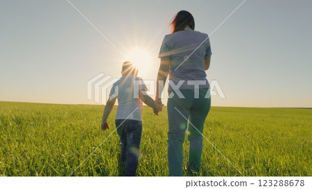 Happy Family Team With Son Walking Together Holding Hands In Green Meadow. Parent Mother With Small Kid Son Walk Through Grass Field Holding Hands At Sunset. Gimbal shot. Happy Family Team With Son Walking Together Holding Hands In Green Meadow. Parent Mother With Small Kid Son Walk Through Grass Field Holding Hands At Sunset. Gimbal shot. 123288678