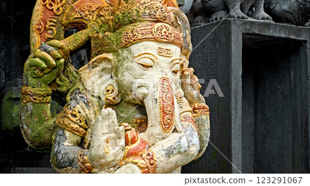 An old stone statue of Ganesha covered with moss, standing on the street An old stone statue of Ganesha covered with moss, standing on the street 123291067