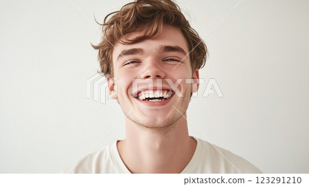 Close-up portrait of a young man with messy brown hair, radiant smile, and joyful expression, set against a plain backdrop. Close-up portrait of a young man with messy brown hair, radiant smile, and joyful expression, set against a plain backdrop. 123291210