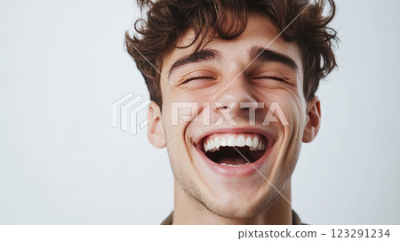 A young man with curly brown hair is bursting with joy, eyes closed, and a wide, radiant smile against a neutral backdrop of white. A young man with curly brown hair is bursting with joy, eyes closed, and a wide, radiant smile against a neutral backdrop of white. 123291234