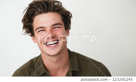 Cheerful young man with tousled brown hair smiles brightly, radiating positivity and joy against a simple white backdrop. 123291245