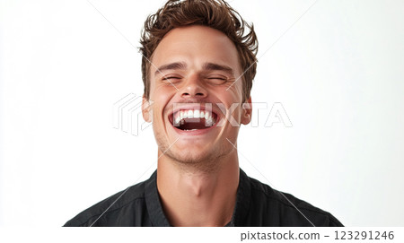 Man with eyes closed and mouth open wide laughs heartily in front of a white backdrop, his dark collared shirt in focus. 123291246