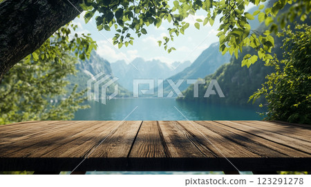 Wooden deck overlooking a serene lake surrounded by lush mountains and greenery on a bright, sunny day, inviting relaxation. 123291278