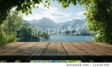 Scenic mountain view with a calm lake, seen through a natural frame of vibrant green foliage with wooden table in the foreground. 123291300